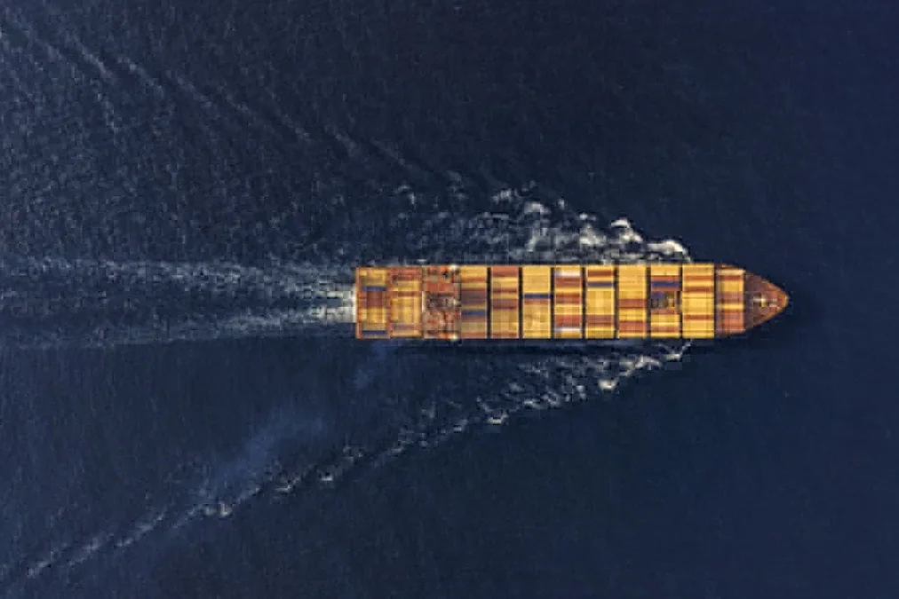 SYZ Weekly Industrial News July 20 2026 SYZ Rod Ends Aerial view of a cargo container ship sailing in dark blue water, leaving a wide wake behind it.